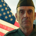A veteran stands beside The American Flag.