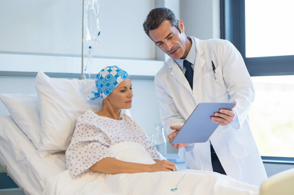 A male doctor is with a female cancer patient lying in a hospital bed.