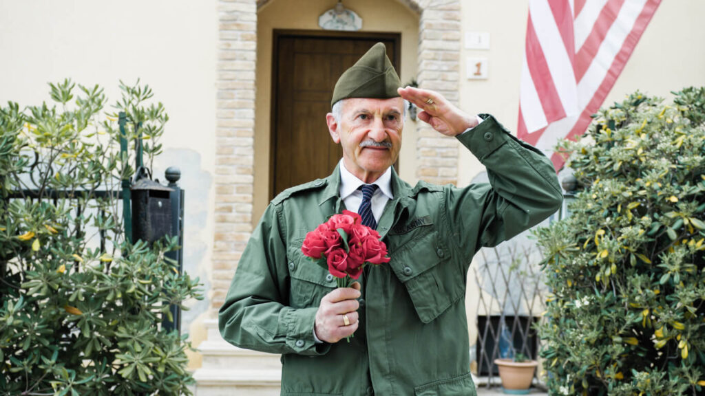 Elderly Veteran Man Salutes In Front Of The American Flag.