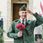 Elderly Veteran Man Salutes In Front Of The American Flag.