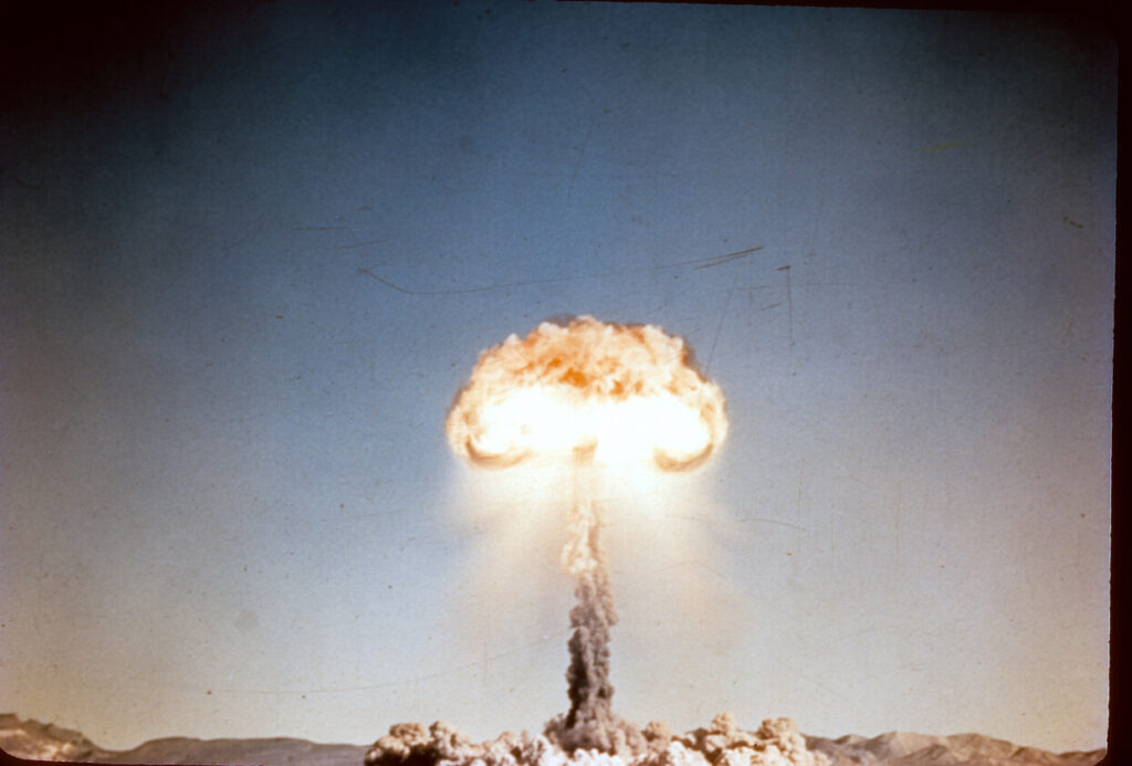 Old slide scan of atom bomb exploding during an atmospheric nuclear test in the desert with red hot fire cloud at the top.