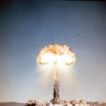 Old slide scan of atom bomb exploding during an atmospheric nuclear test in the desert with red hot fire cloud at the top.